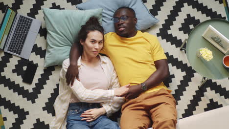 Diverse-Couple-Lying-on-Floor-and-Looking-at-Camera